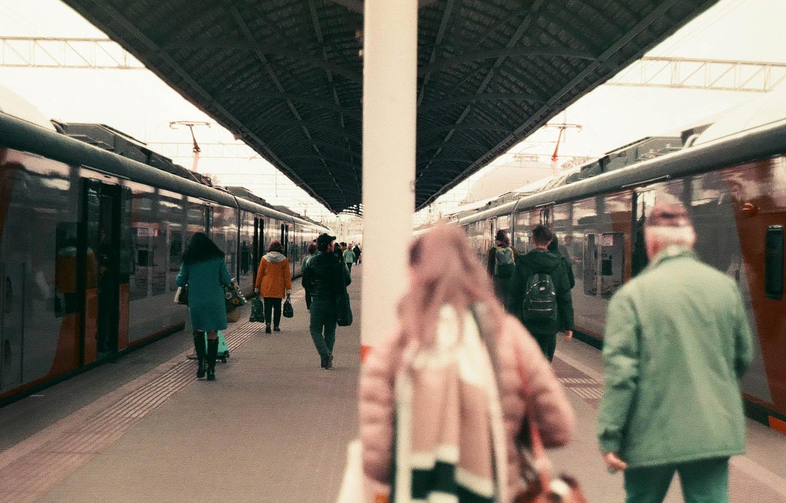 Большая группа людей идёт по железнодорожной платформе между двух электричек